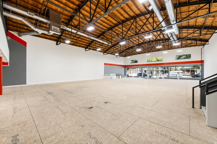 Expansive commercial space featuring exposed wood beam ceilings, overhead lighting, and extensive street-facing windows