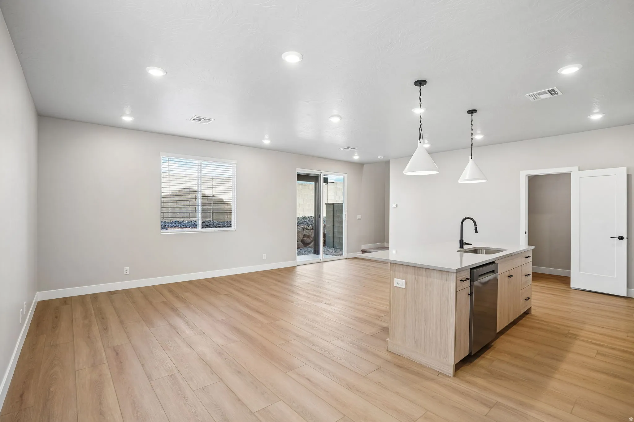 Kitchen island with integrated sink, stainless steel dishwasher, and pendant lighting