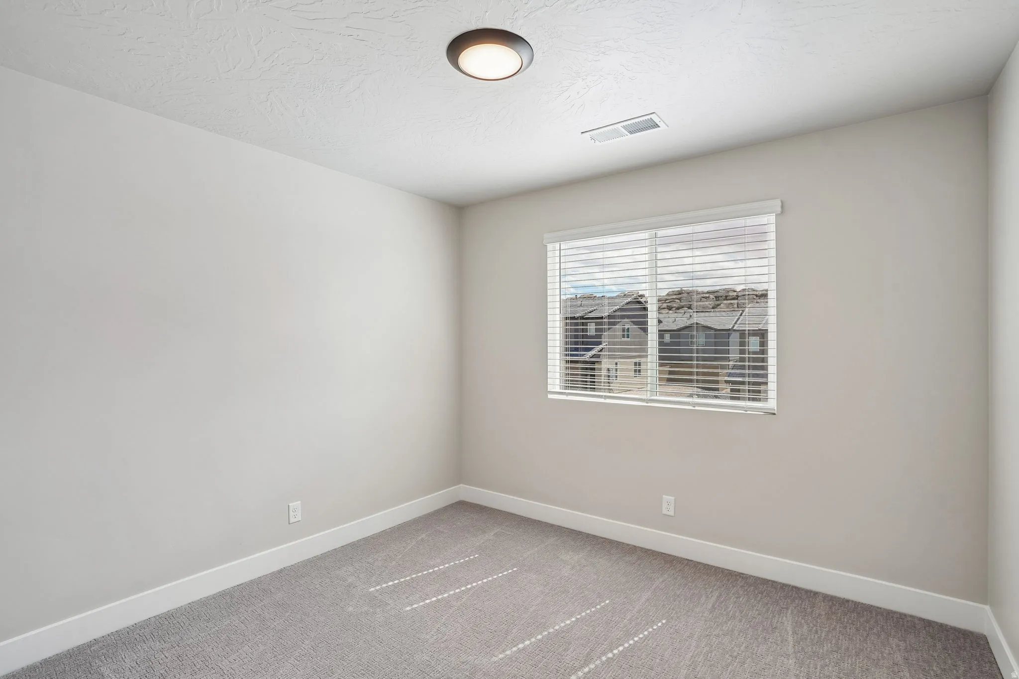 Neutral wall tones, gray carpeting, and a window with blinds