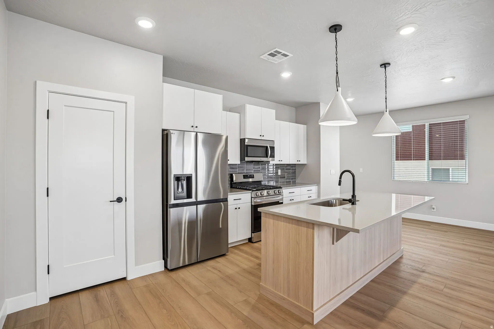 Modern kitchen featuring stainless steel appliances, white cabinetry, a kitchen island with sink and matte black faucet, wood-finish flooring, and recessed lighting