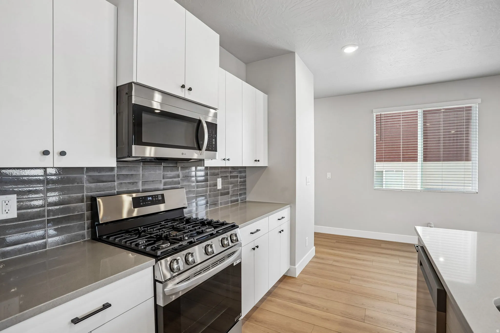 Modern kitchen featuring white cabinetry, stainless steel appliances, a dark subway tile backsplash, and light wood-finish flooring