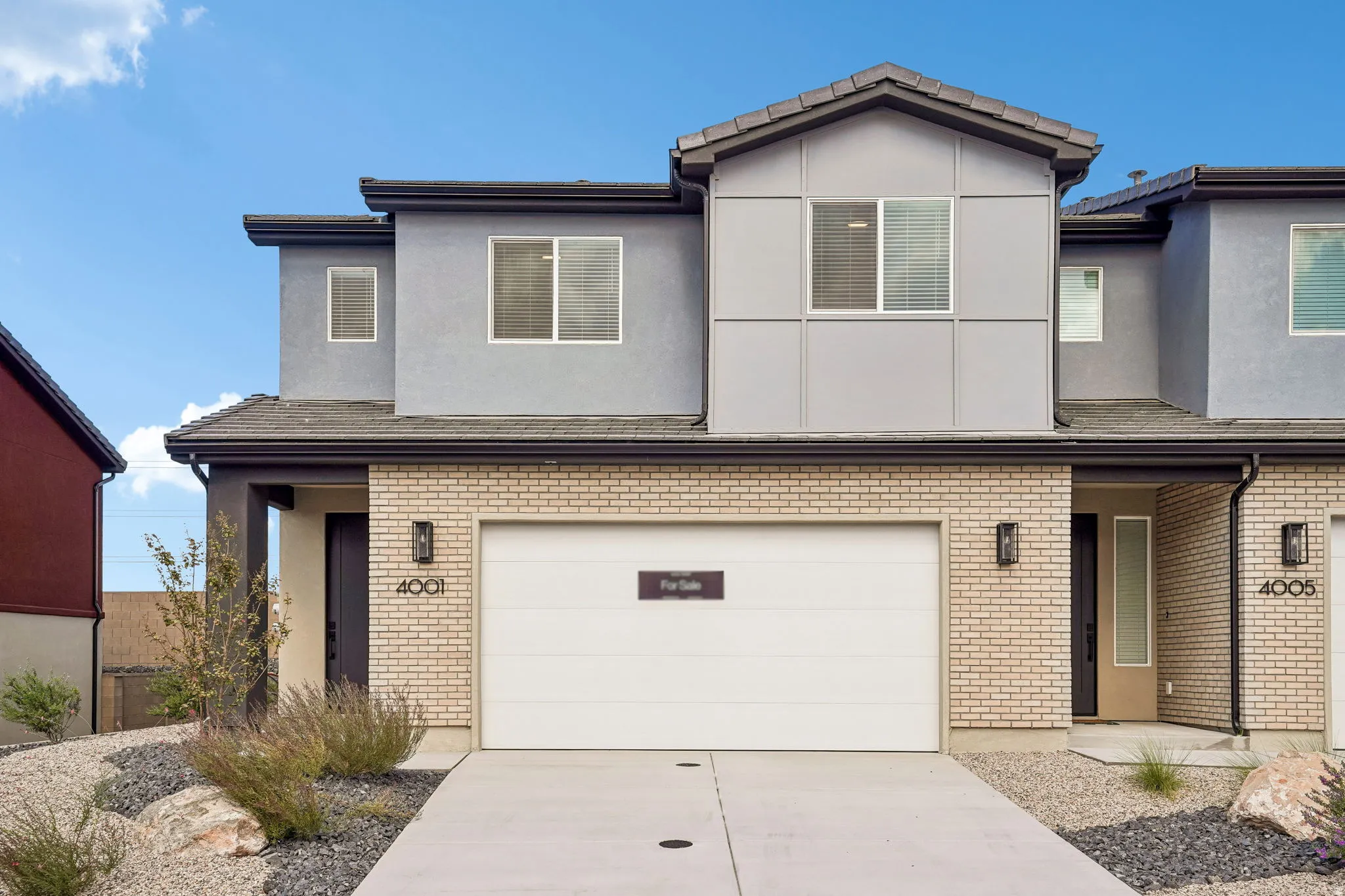 Contemporary exterior featuring light brick, gray siding, a two-car garage, and modern exterior lighting