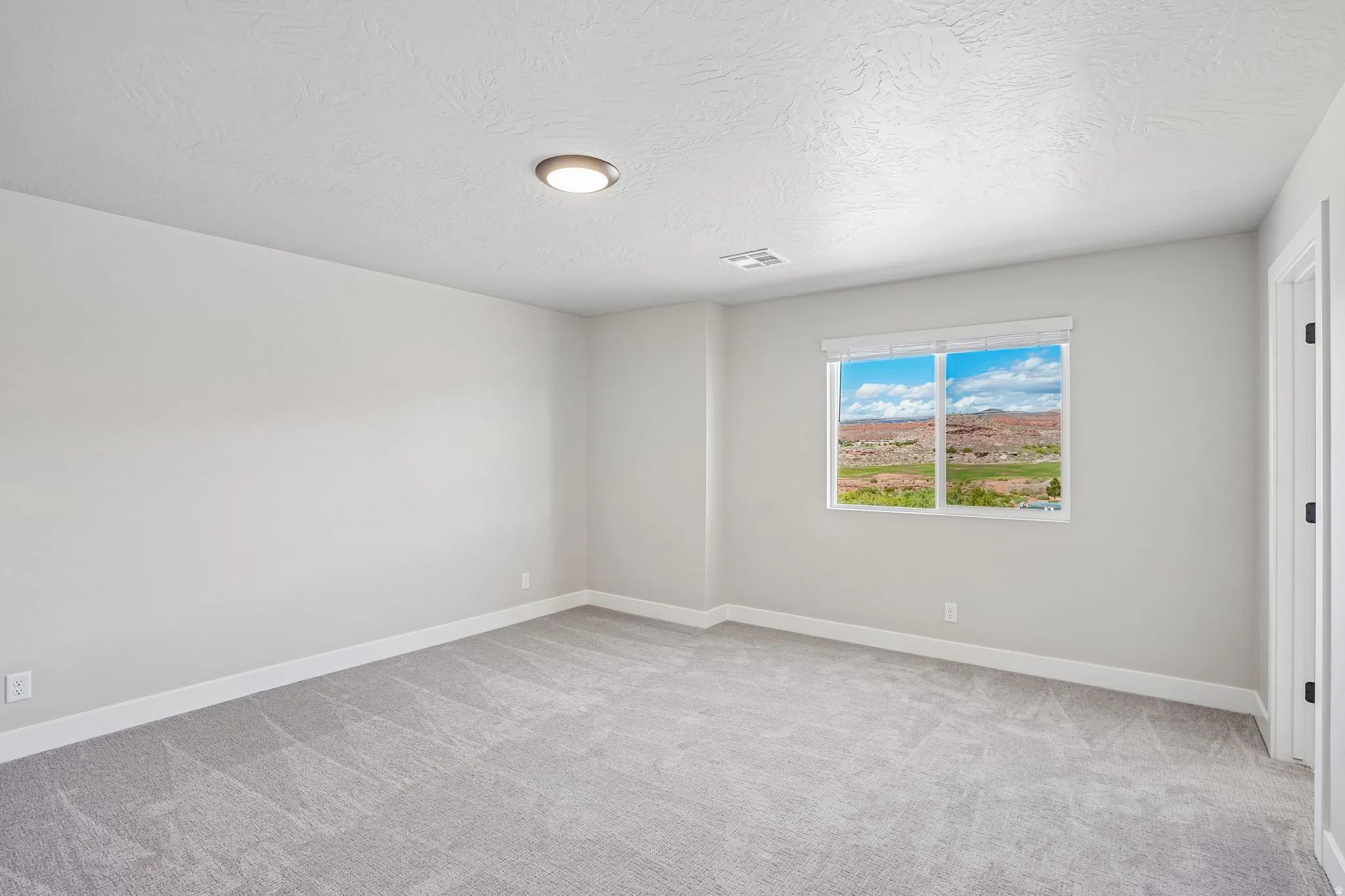 Spacious room featuring light gray carpeting, neutral wall finishes, a large window with white framing, and a recessed ceiling light