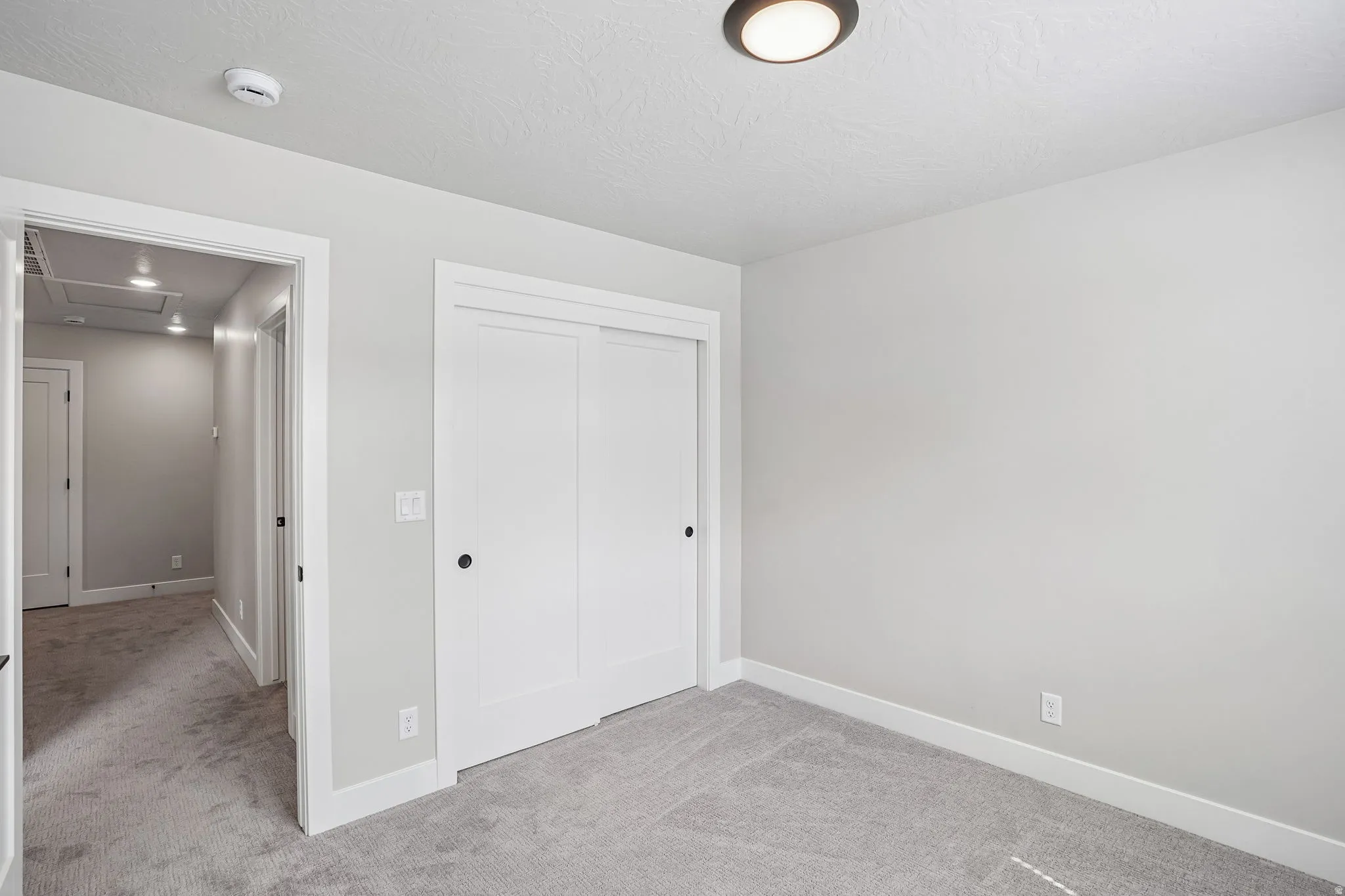 Carpeted room with white sliding closet doors, white trim, and a flush mount ceiling light fixture