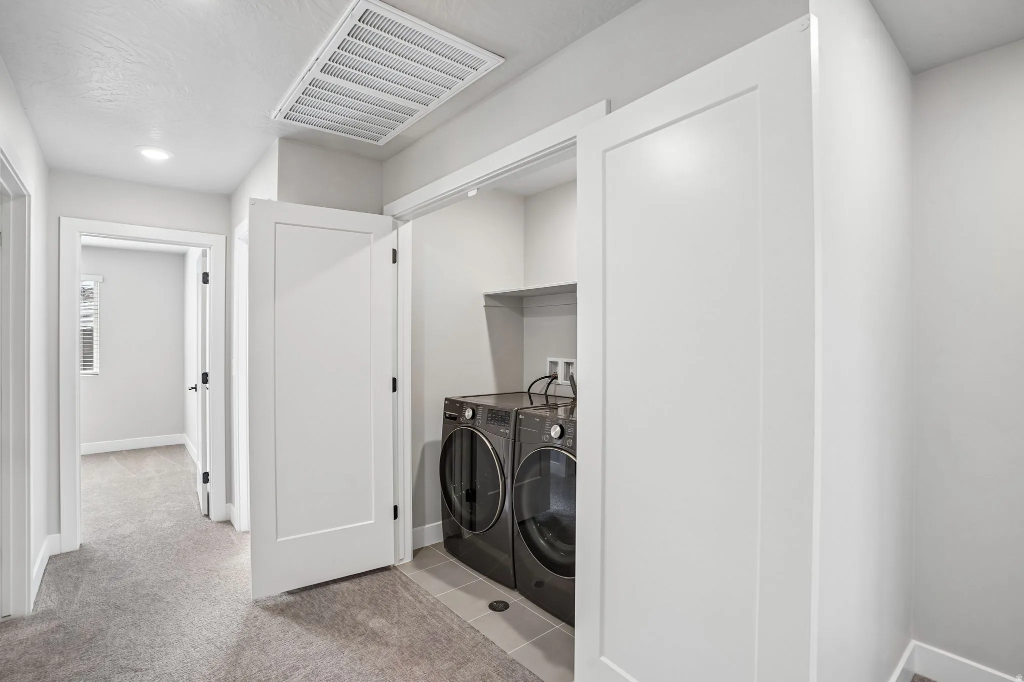 Laundry closet with tile flooring and a built-in shelf, featuring adjacent carpeted hallway