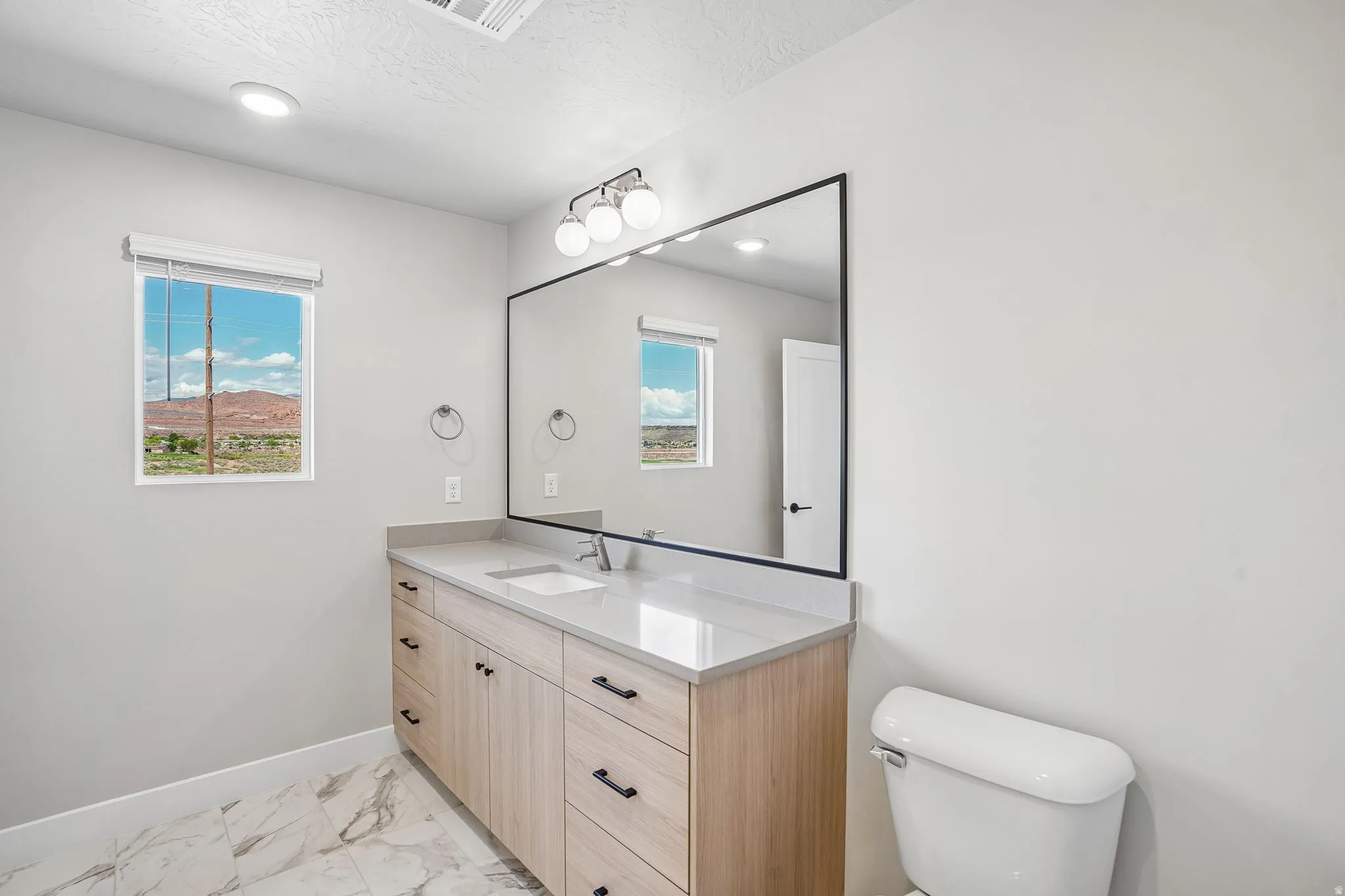 Light-toned wood-finish vanity with a light countertop, undermount sink, and black hardware