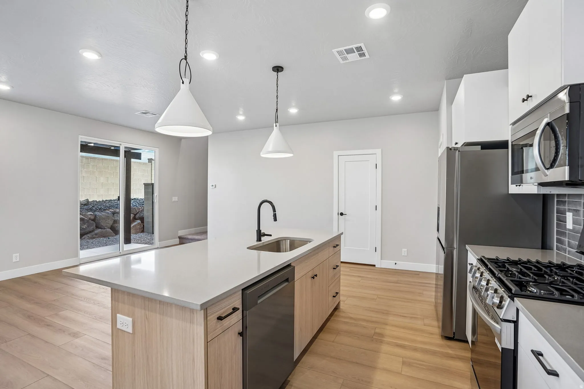 Kitchen featuring a large central island with light-toned cabinetry, stainless steel appliances, and wood-finish flooring