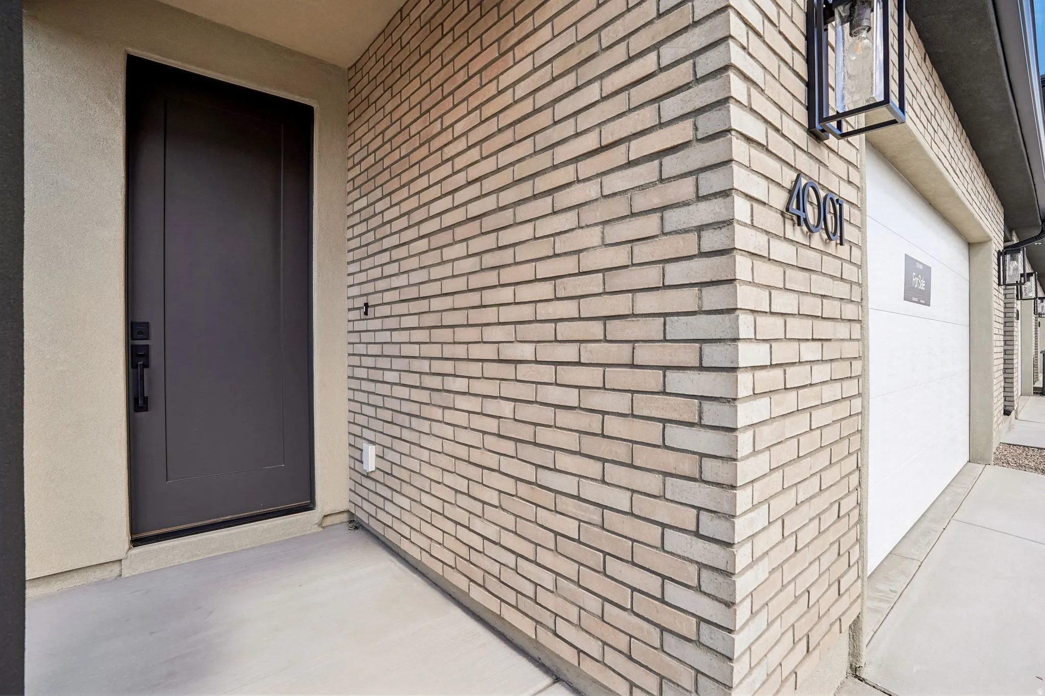 Brick exterior with stucco accents, dark entry door with matte black hardware, and an attached garage with modern exterior lighting