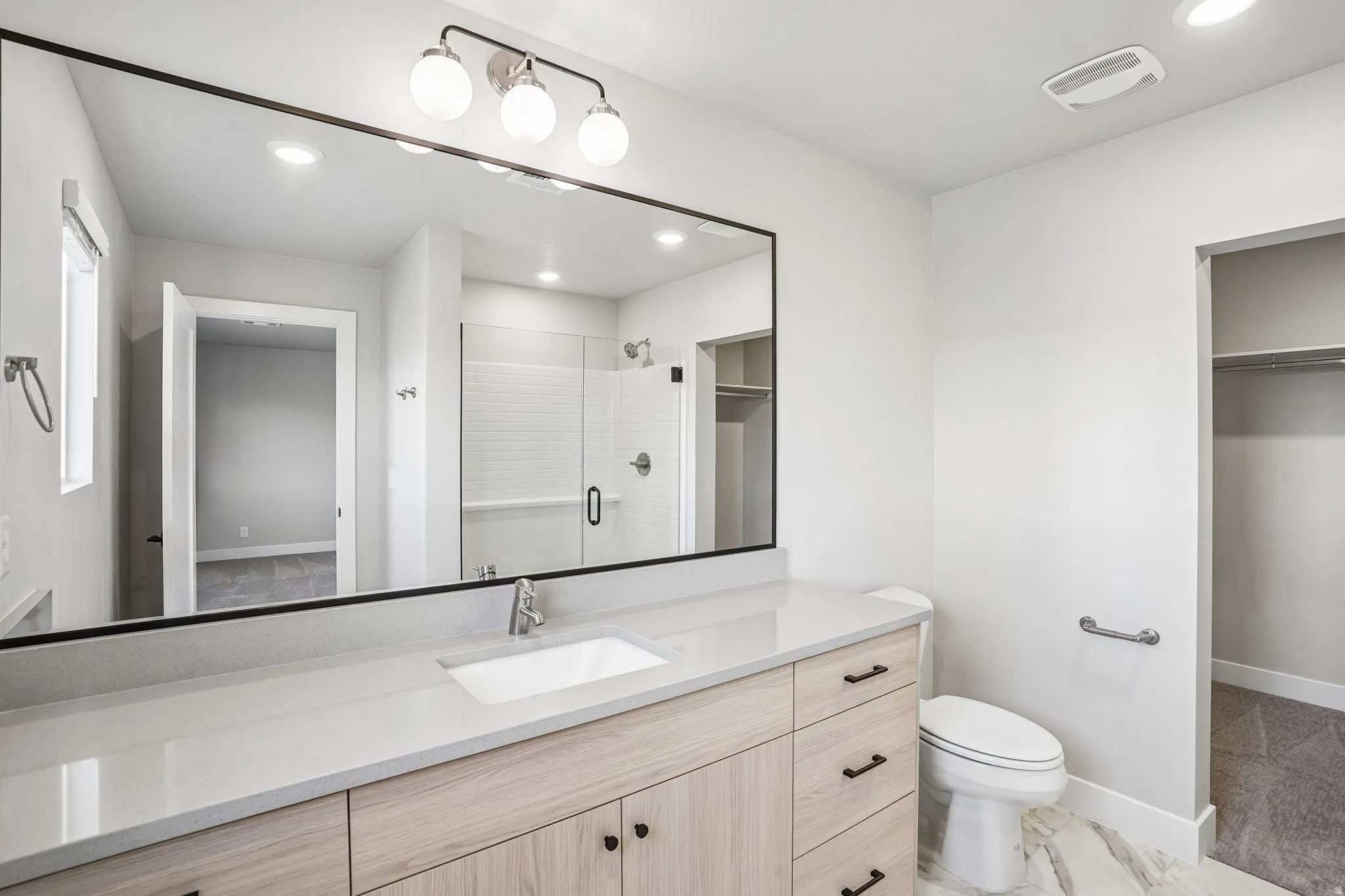 Modern bathroom featuring a wood-finish vanity with a light-toned countertop, an integrated rectangular sink, a large wall-mounted mirror, and a glass-enclosed shower with subway tile