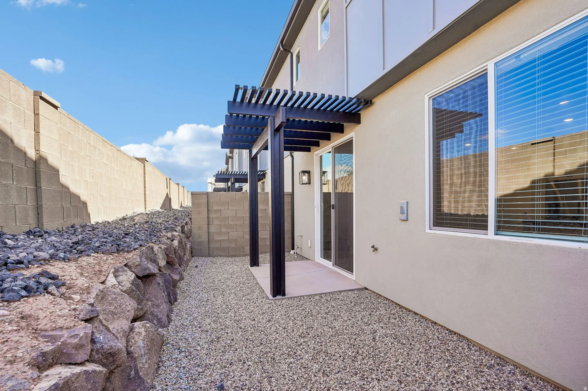 Pergola-covered patio featuring sliding glass doors, a gravel ground covering, and a rock retaining wall