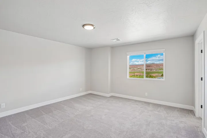 Spacious room featuring light gray carpeting, neutral wall finishes, a large window with white framing, and a recessed ceiling light