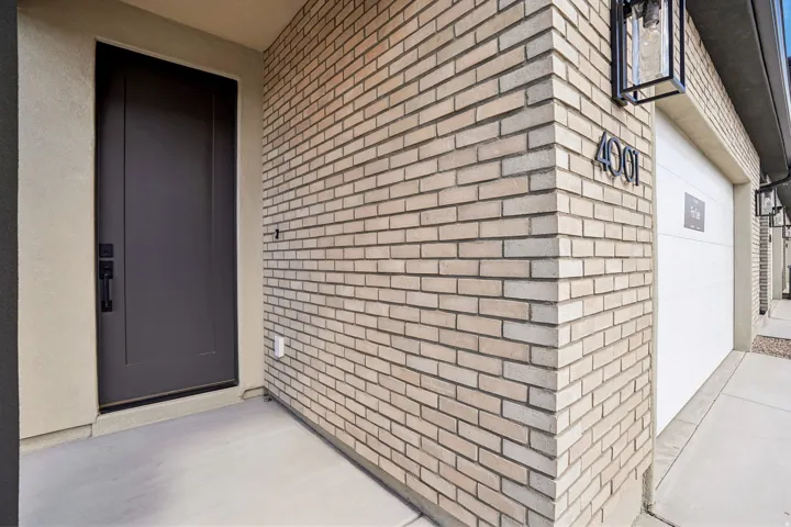 Brick exterior with stucco accents, dark entry door with matte black hardware, and an attached garage with modern exterior lighting