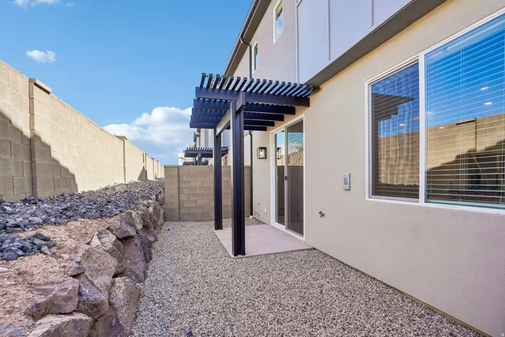 Pergola-covered patio featuring sliding glass doors, a gravel ground covering, and a rock retaining wall