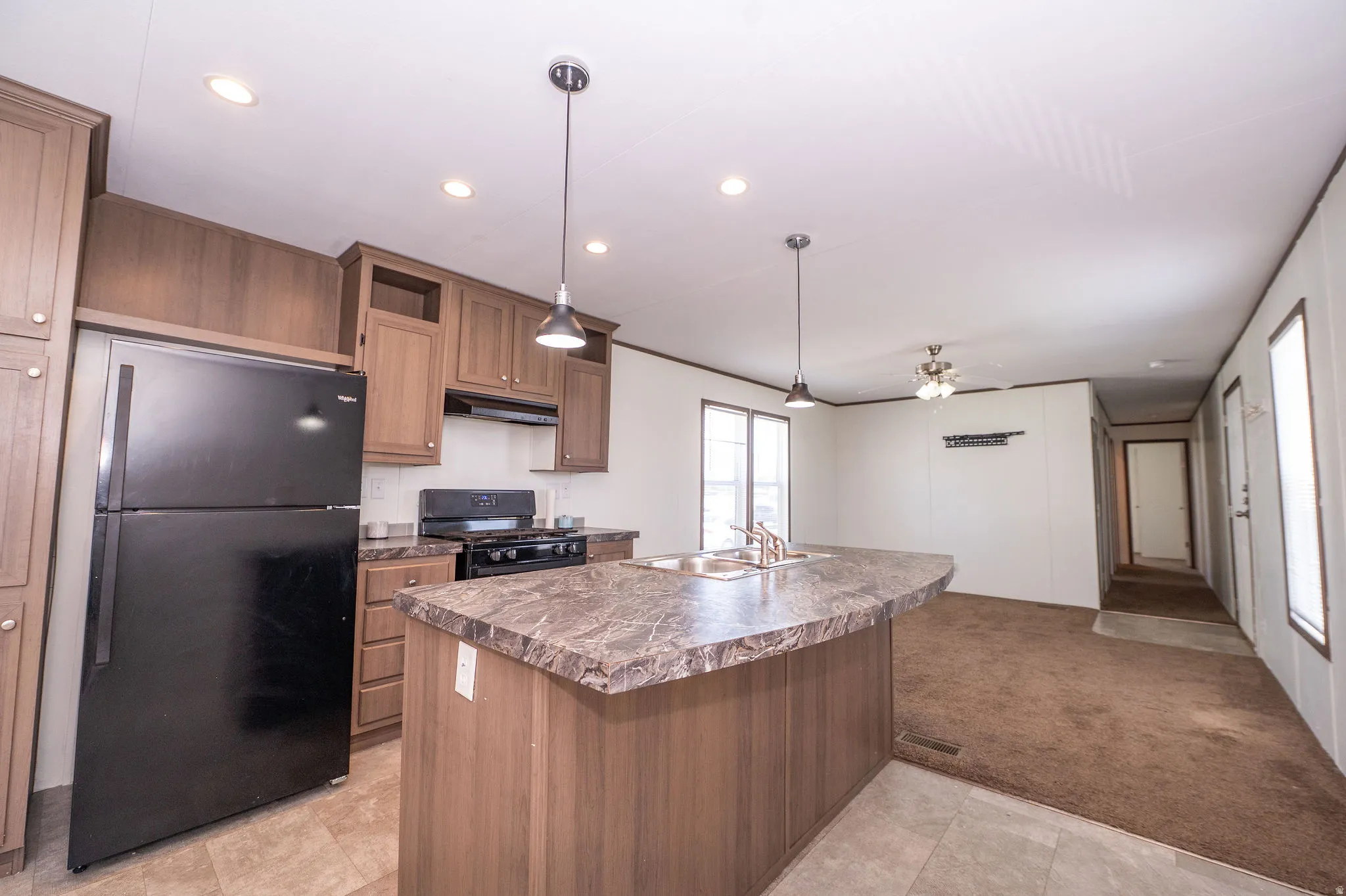 Open concept kitchen featuring wood-finish cabinetry, black appliances, a large island with a double sink, and pendant lighting