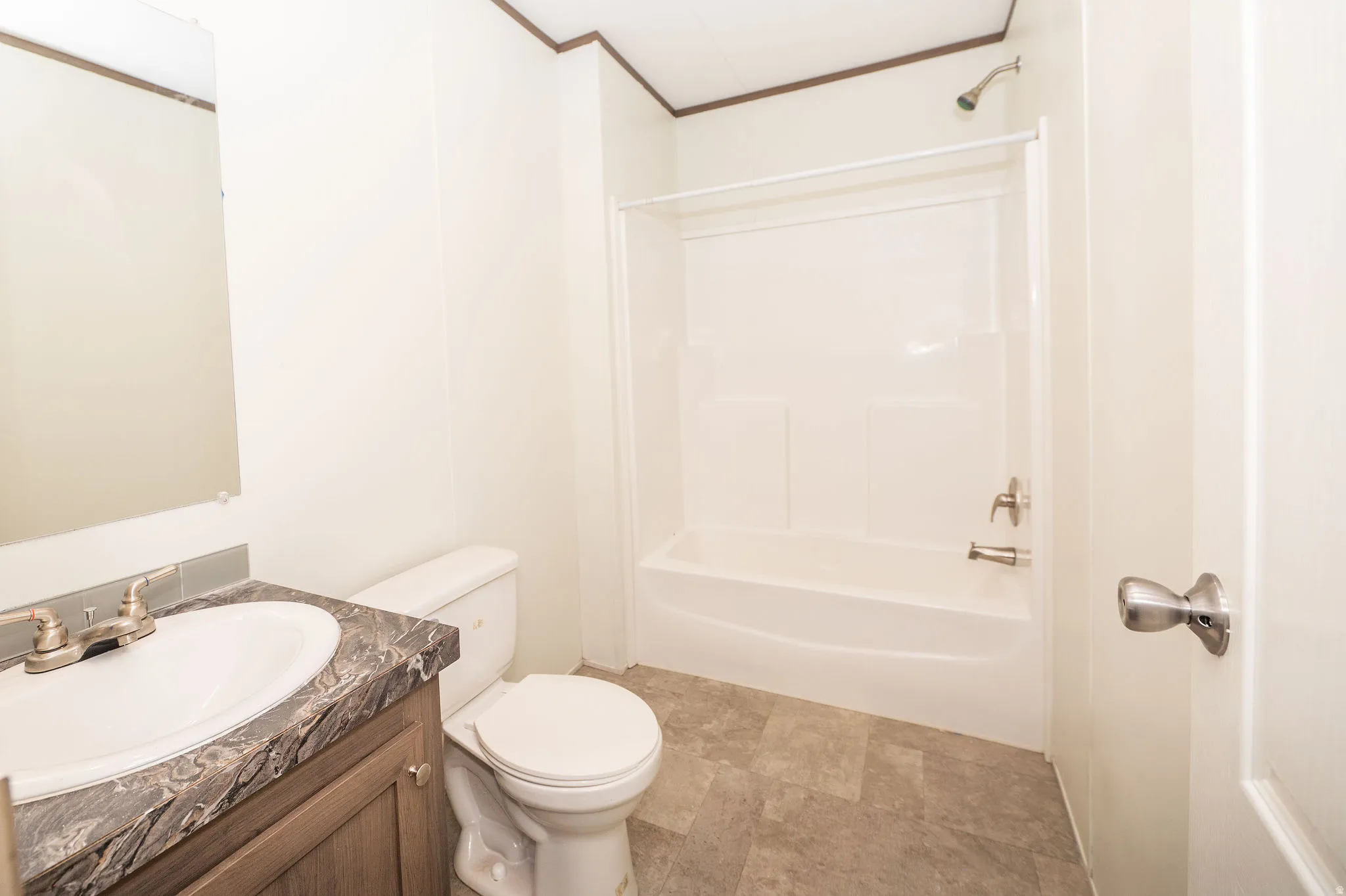 Bathroom featuring a vanity with an integrated sink, a dark patterned countertop, wood-finish cabinetry, a white toilet, and a white shower/tub combination with a chrome shower head and faucet