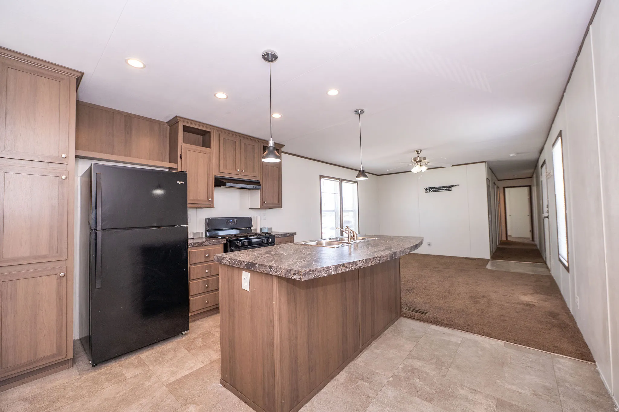 Kitchen featuring wood-finish cabinetry, black appliances, a gas range, and a large island with an integrated sink and pendant lighting