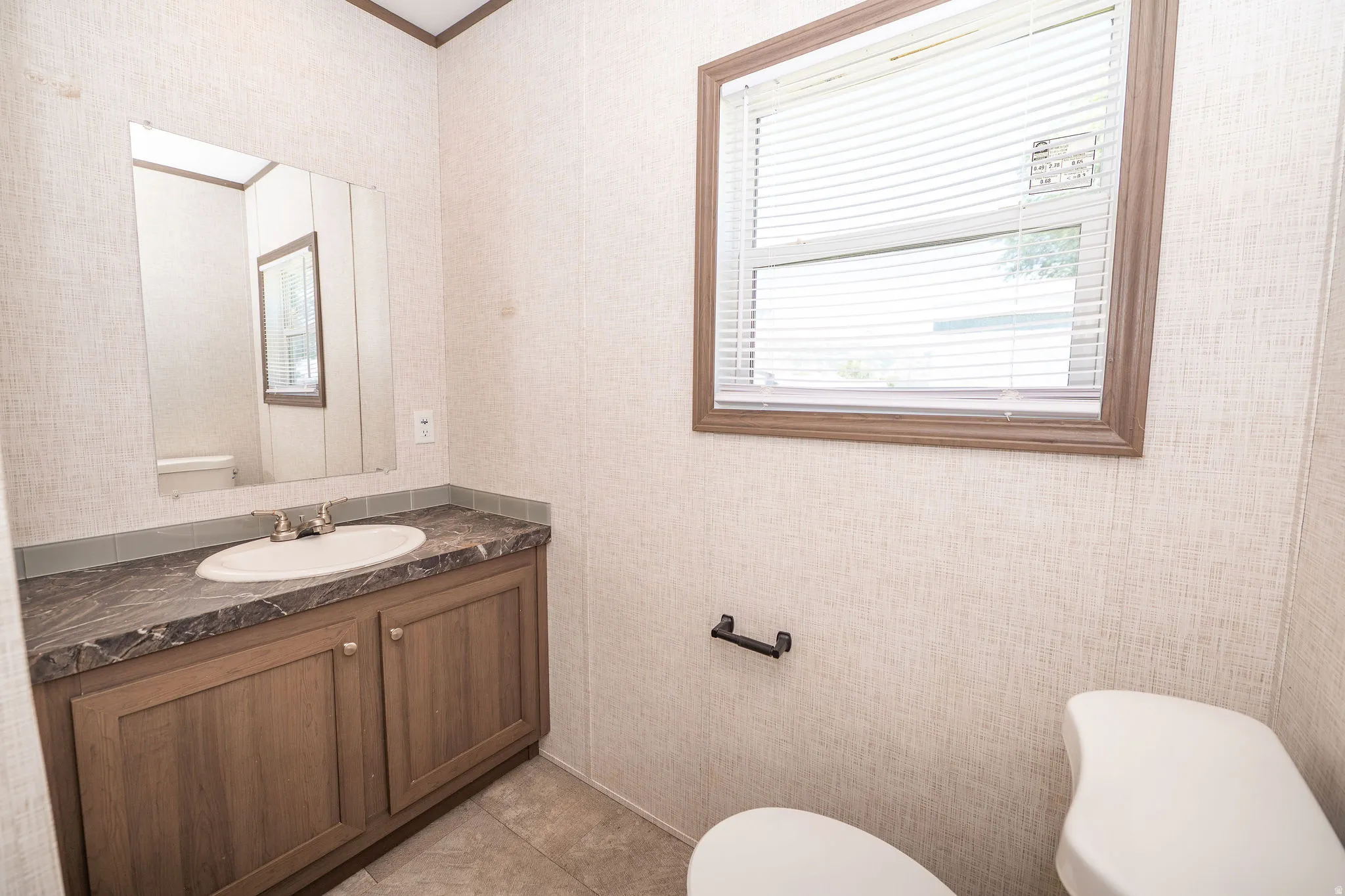 Bathroom vanity with wood-finish cabinetry, a white basin, and a dark patterned countertop