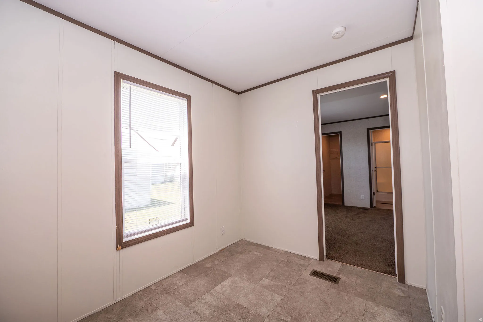 Room featuring a window with blinds, paneling walls, brown trim, and tile flooring
