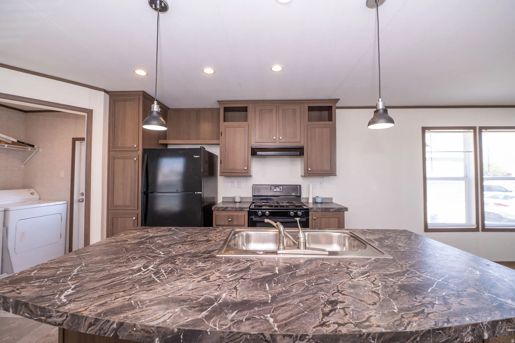 Kitchen island featuring a double basin stainless steel sink with a chrome faucet, dark marbled countertop, and two pendant lights