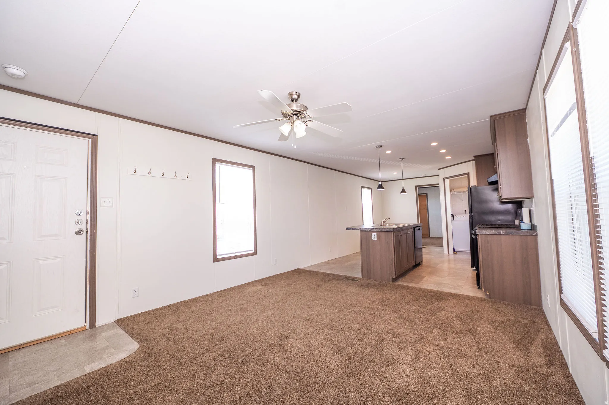 Open-concept living area featuring a ceiling fan with light fixture, a kitchen island with pendant lighting, wood-finish cabinetry, black appliances, and a window with blinds