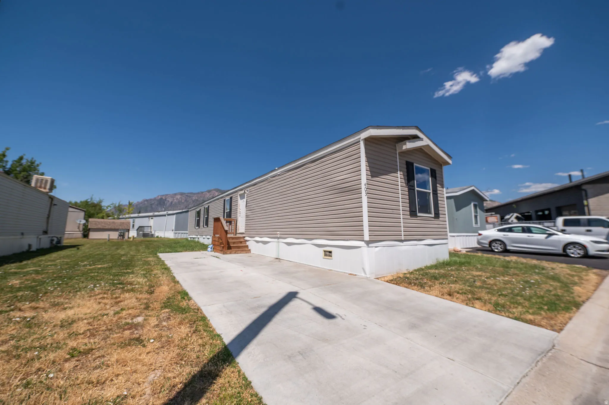 Manufactured home with light brown horizontal siding, a white foundation, and a dark brown wooden entry staircase