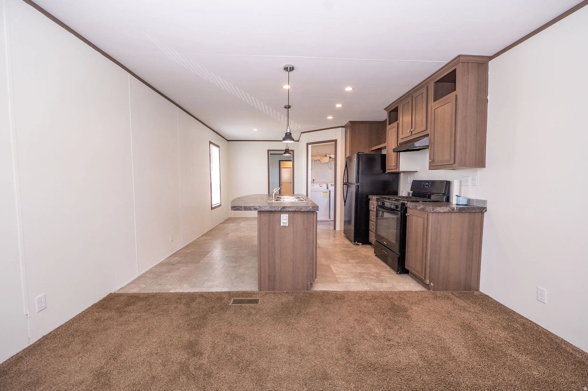 Open-concept living space featuring a kitchen with black appliances, wood-finish cabinetry, and a peninsula with a sink and pendant lighting