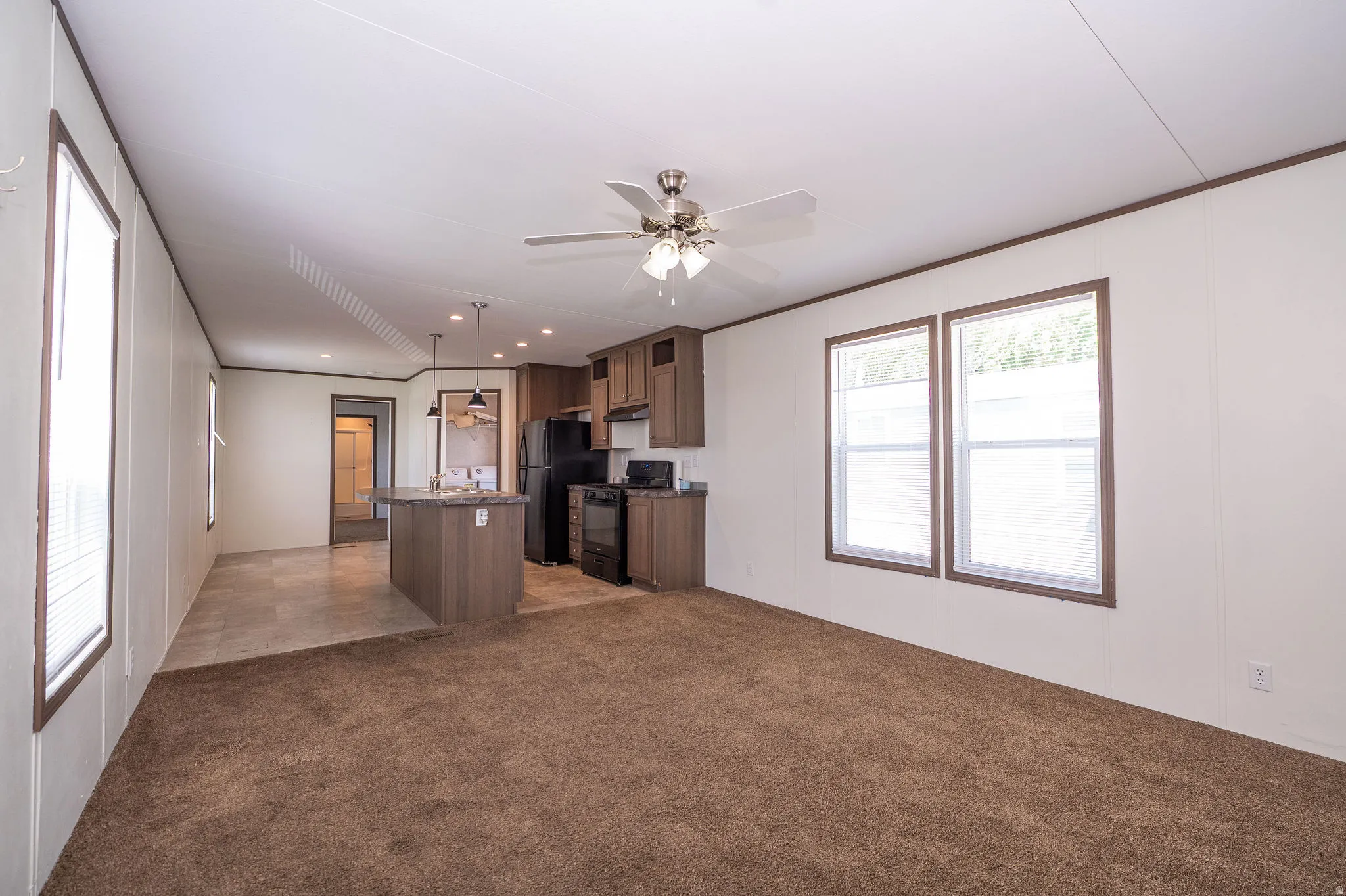 Open-concept living area featuring a kitchen island with pendant lighting, integrated black appliances, wood-finish cabinetry, and a ceiling fan