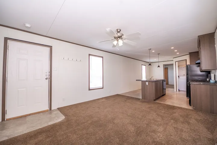 Open-concept living area featuring a ceiling fan with integrated lighting, a kitchen island with pendant lighting, dark wood-finish cabinetry, and a black appliance suite