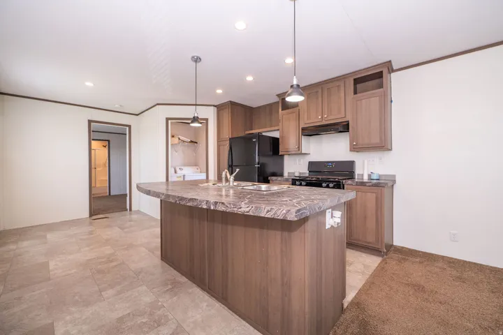 Kitchen featuring a central island with an integrated sink, wood-finish cabinetry, black appliances, and pendant lighting