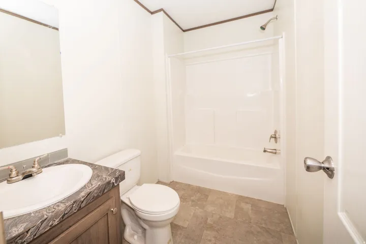 Bathroom featuring a vanity with an integrated sink, a dark patterned countertop, wood-finish cabinetry, a white toilet, and a white shower/tub combination with a chrome shower head and faucet