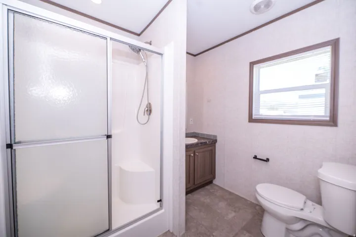 Bathroom featuring a shower with sliding opaque glass doors and a built-in seat, a wood-finish vanity with an integrated sink and dark countertop, a window with horizontal blinds, and a toilet