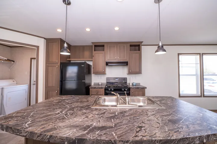 Kitchen island featuring a double basin stainless steel sink with a chrome faucet, dark marbled countertop, and two pendant lights