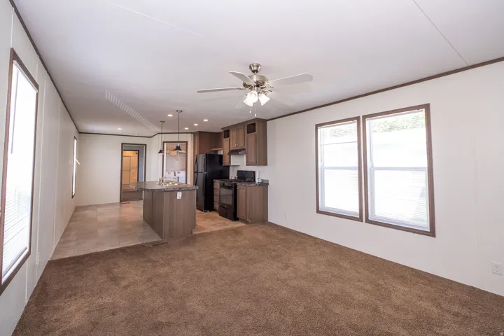 Open-concept living space featuring a kitchen island with pendant lighting, black appliances, wood-finish cabinetry, and a ceiling fan