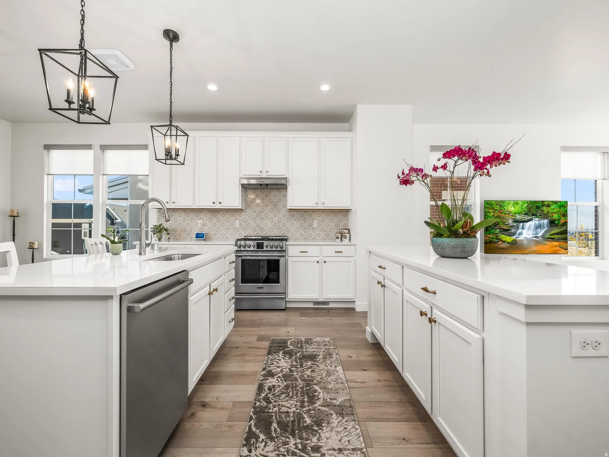 Bright kitchen featuring two white islands with stone countertops, stainless steel appliances, white cabinetry, and wood-finish flooring
