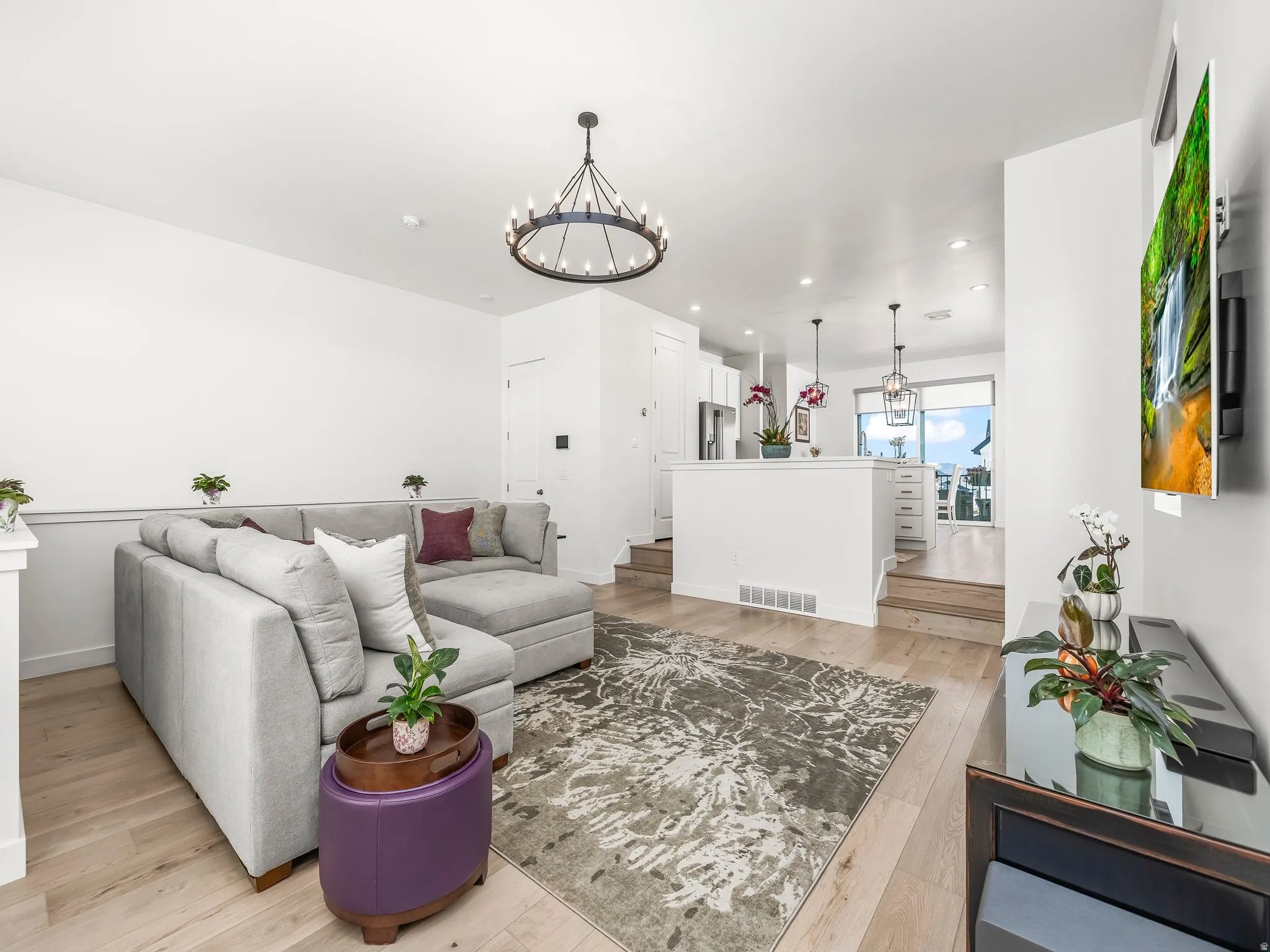 Open-concept living area featuring light wood-finish flooring, a contemporary chandelier, and wainscoting