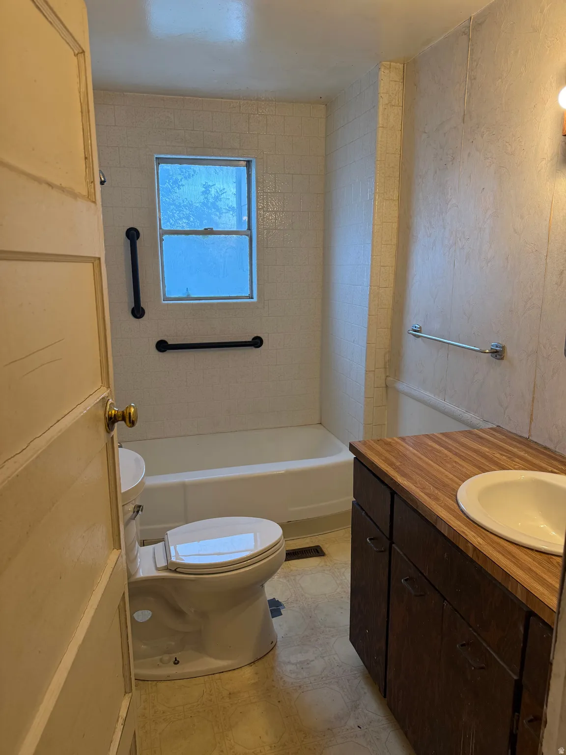 Bathroom featuring a tub with white tile surround, window, toilet, and wood-finish vanity with an integrated sink