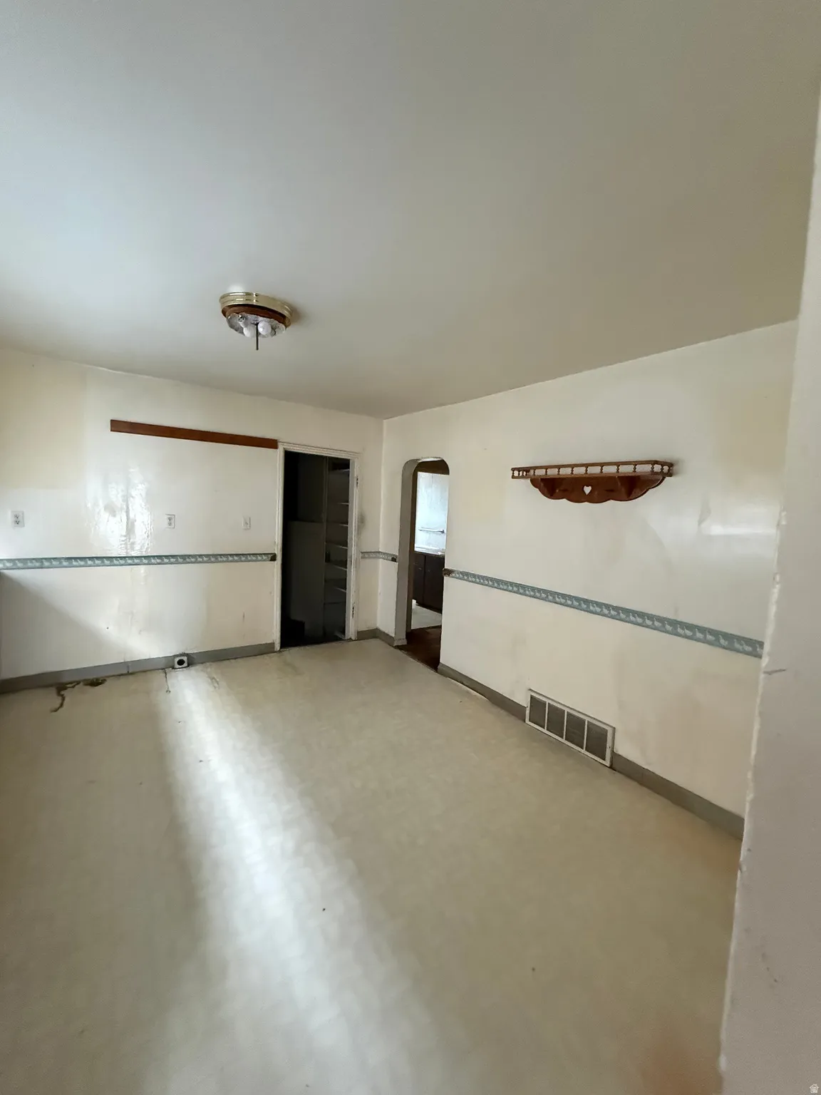 Spacious room featuring light-colored flooring, neutral wall tones with decorative trim, and an overhead flush-mount light fixture