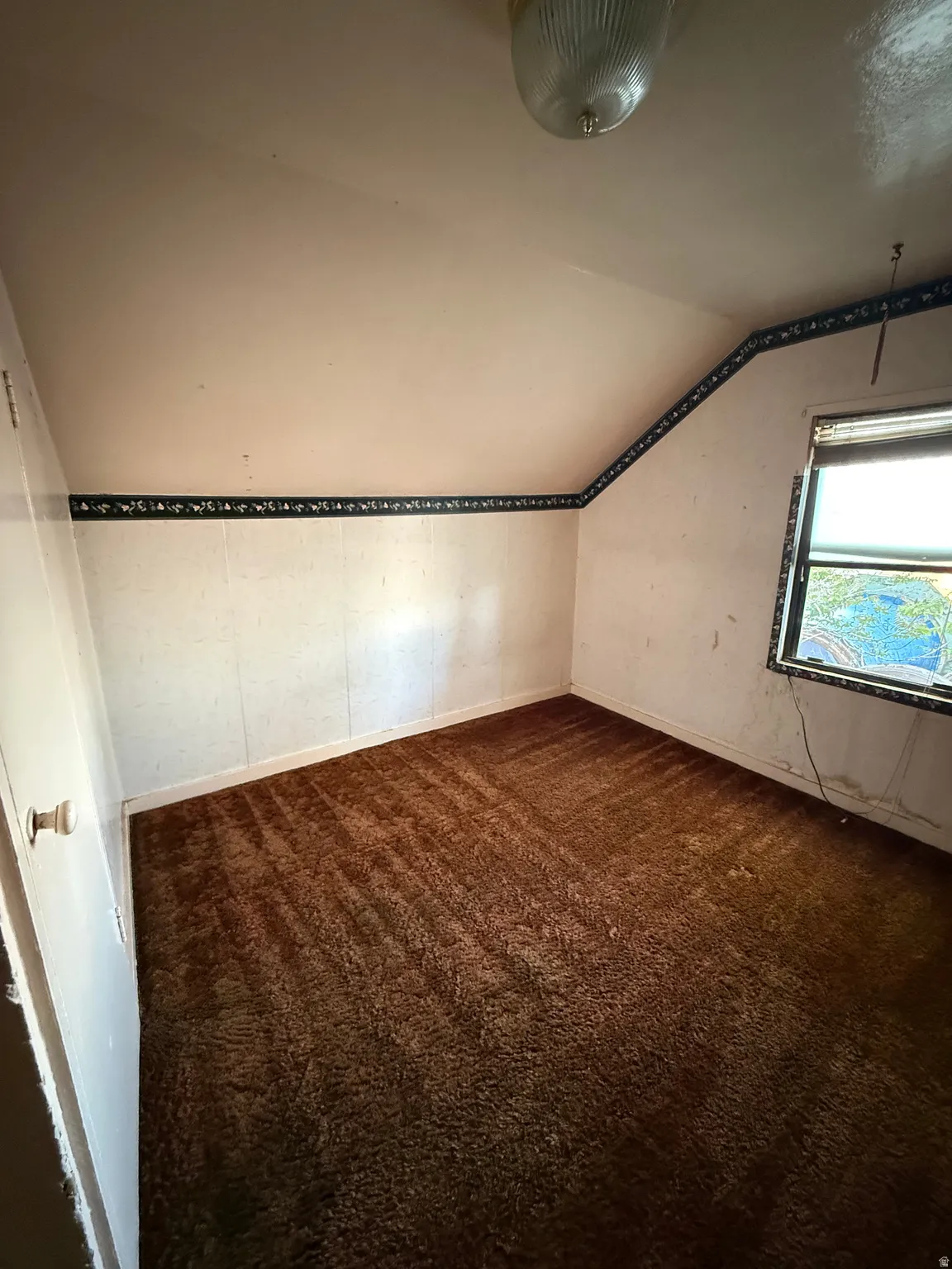 Carpeted room with a pitched ceiling and a single window