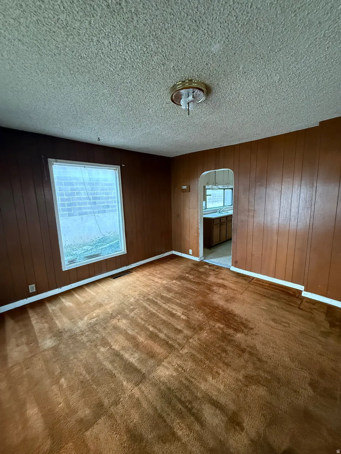 Interior space featuring vertical wood paneling, a single window, and textured ceiling
