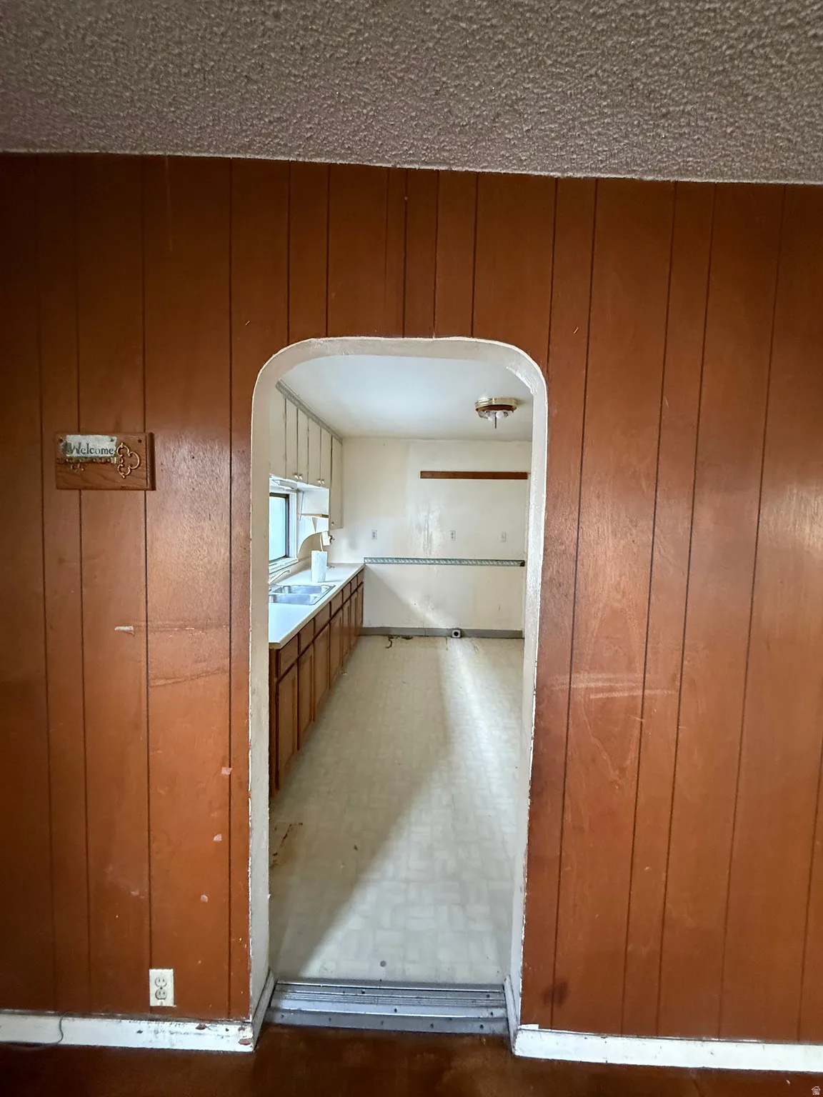 Kitchen featuring wood-finish lower cabinetry, a double basin stainless steel sink, and light-toned flooring