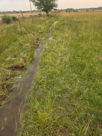 Natural water feature meandering through expansive green pasture