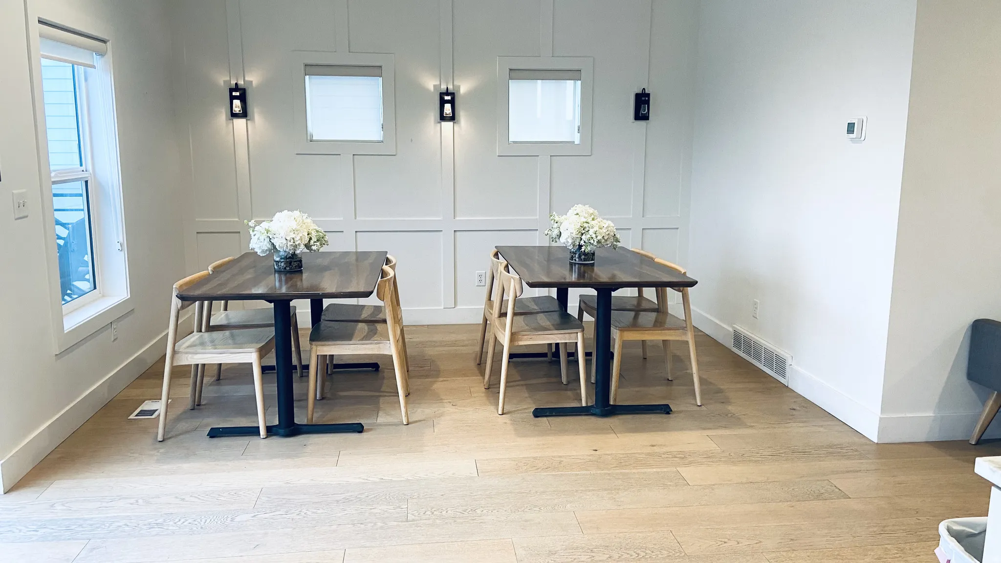 Wood-finish flooring throughout, white paneled accent wall, two fixed windows, and two wall-mounted sconces