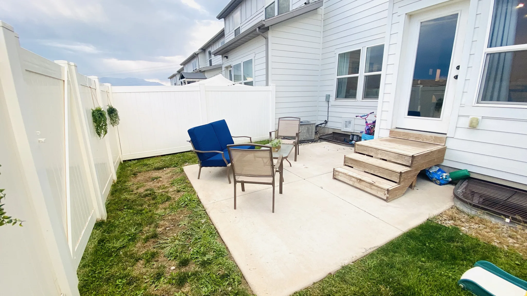 Spacious concrete patio with direct access to the residence, complemented by a manicured lawn, white vinyl privacy fencing, and mature landscaping