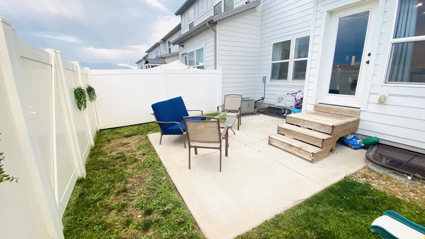 Spacious concrete patio with direct access to the residence, complemented by a manicured lawn, white vinyl privacy fencing, and mature landscaping