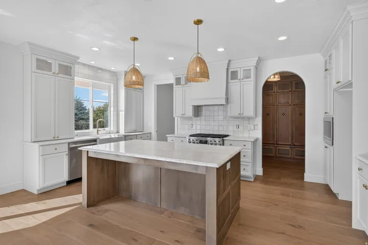 Spacious kitchen featuring an expansive center island with a light-toned countertop, wood-finish flooring, white cabinetry, and stainless steel appliances