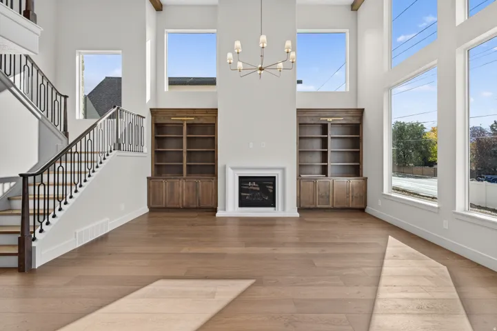 Vaulted ceilings with exposed beams, wood-finish flooring, a built-in gas fireplace with white mantel, custom built-in cabinetry, and a striking chandelier