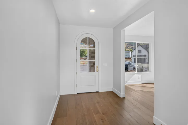 Arched glass-paneled entry door, wood-finish flooring, recessed ceiling lighting, and a wide cased opening