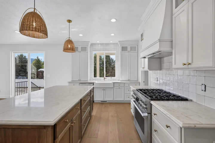 Spacious kitchen featuring an expansive center island with countertop, hardwood flooring, white cabinetry, and a professional-grade range