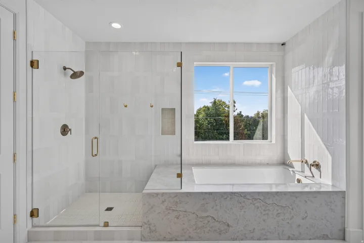 Contemporary bathroom featuring a spacious glass-enclosed shower, a built-in soaking tub, a large window, and light-toned tilework throughout