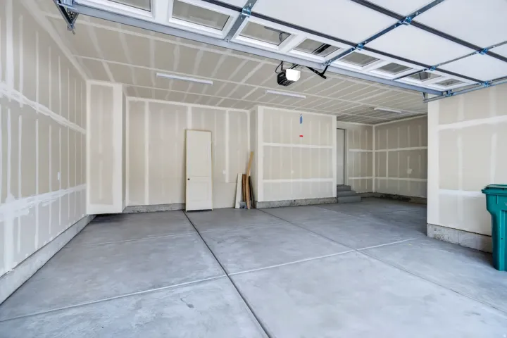 Expansive garage space with a concrete floor, exposed ceiling framework, and fluorescent lighting fixtures
